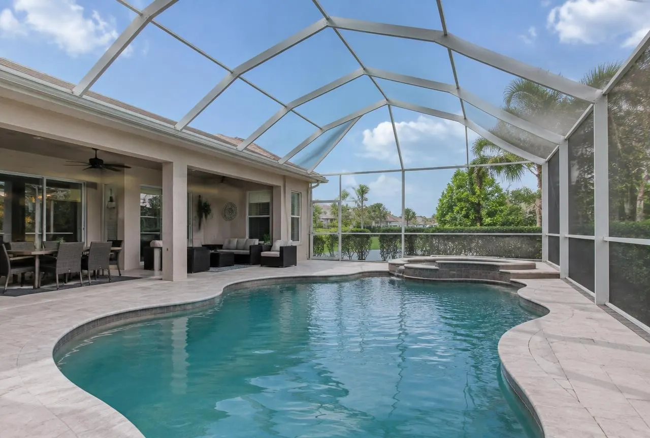 White aluminum pool cage over a curved pool beside a Florida home